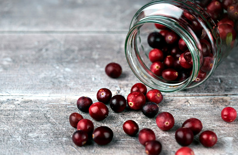 A jar of cranberries on is side. A few cranberries are spread out on the table. 